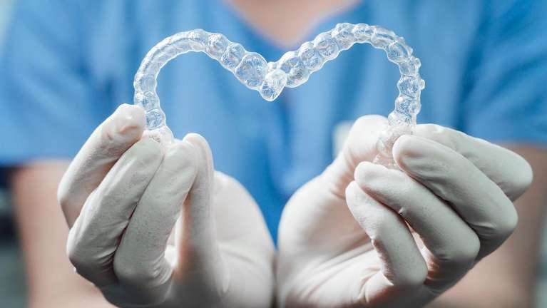 dentist holding clear plastic aligners | invisalign parramatta